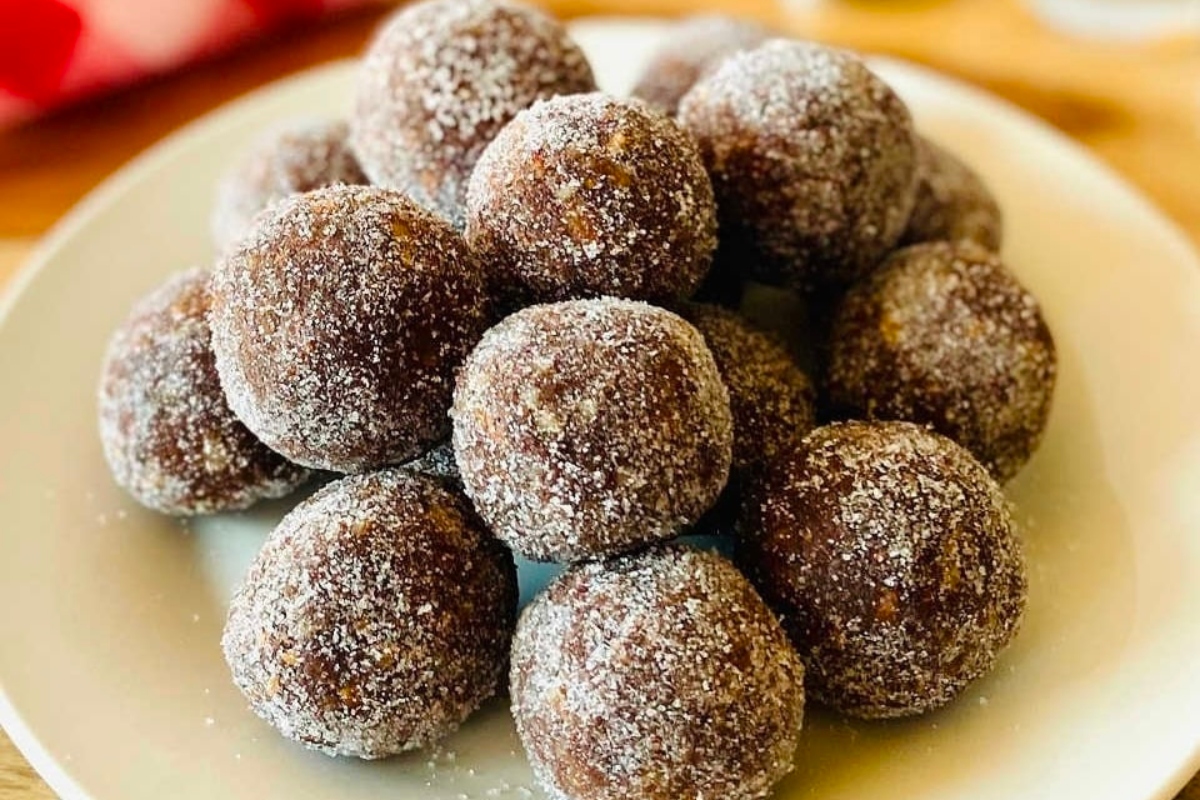 A plate full of sugared balls, a delightful no bake Christmas dessert, on a wooden table.