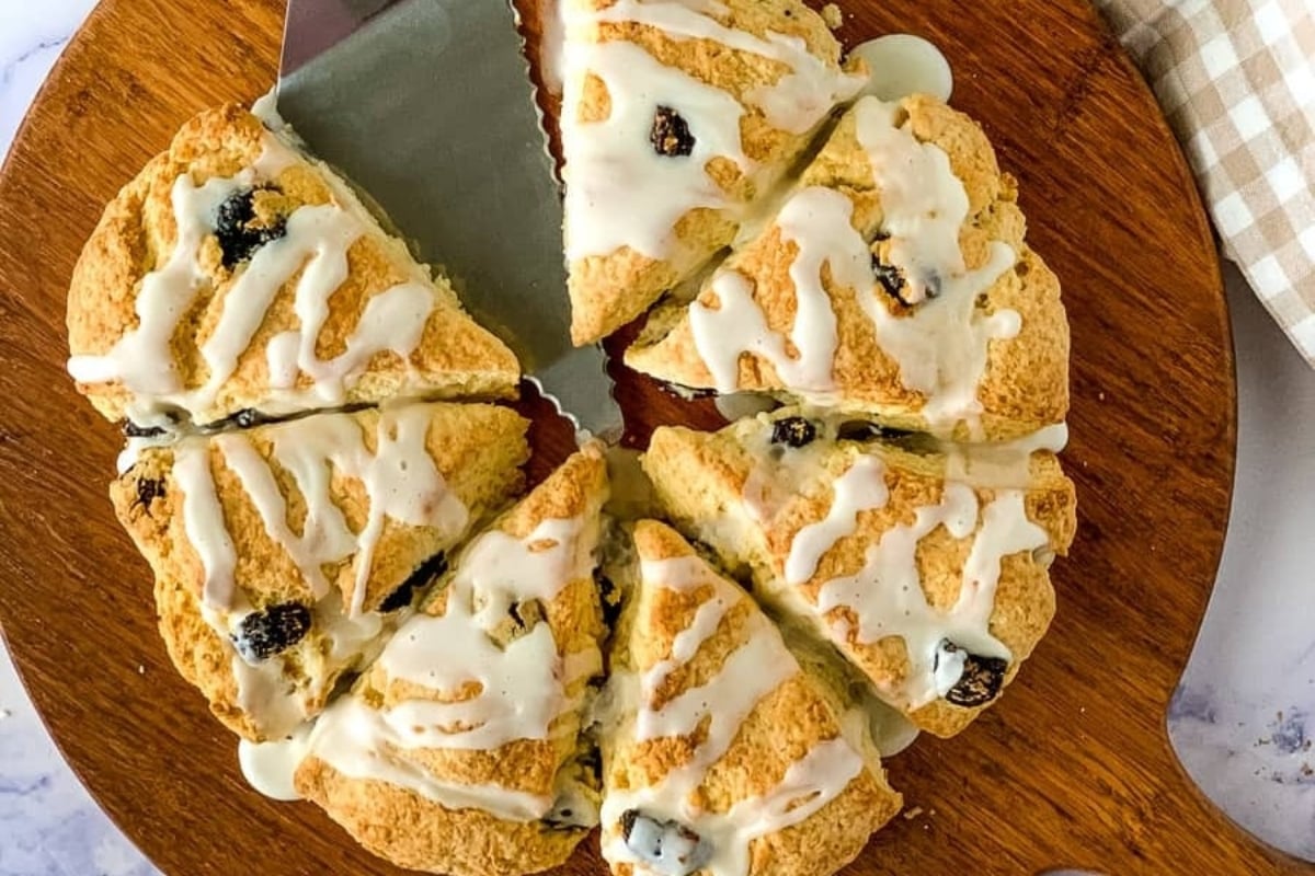 Cranberry scones with icing and a knife on a wooden cutting board.