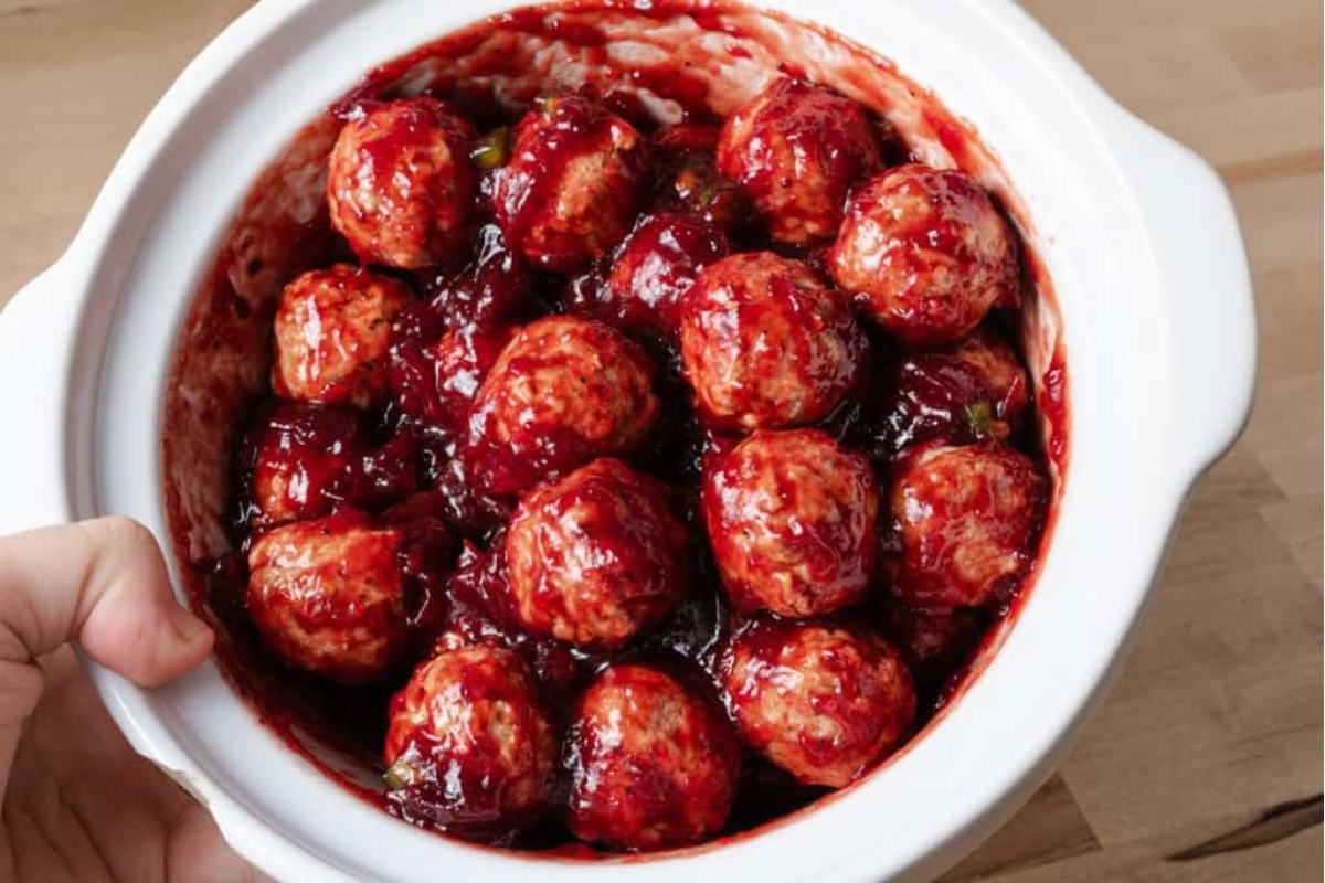 Festive cranberry meatballs slow-cooked in a white crock pot.