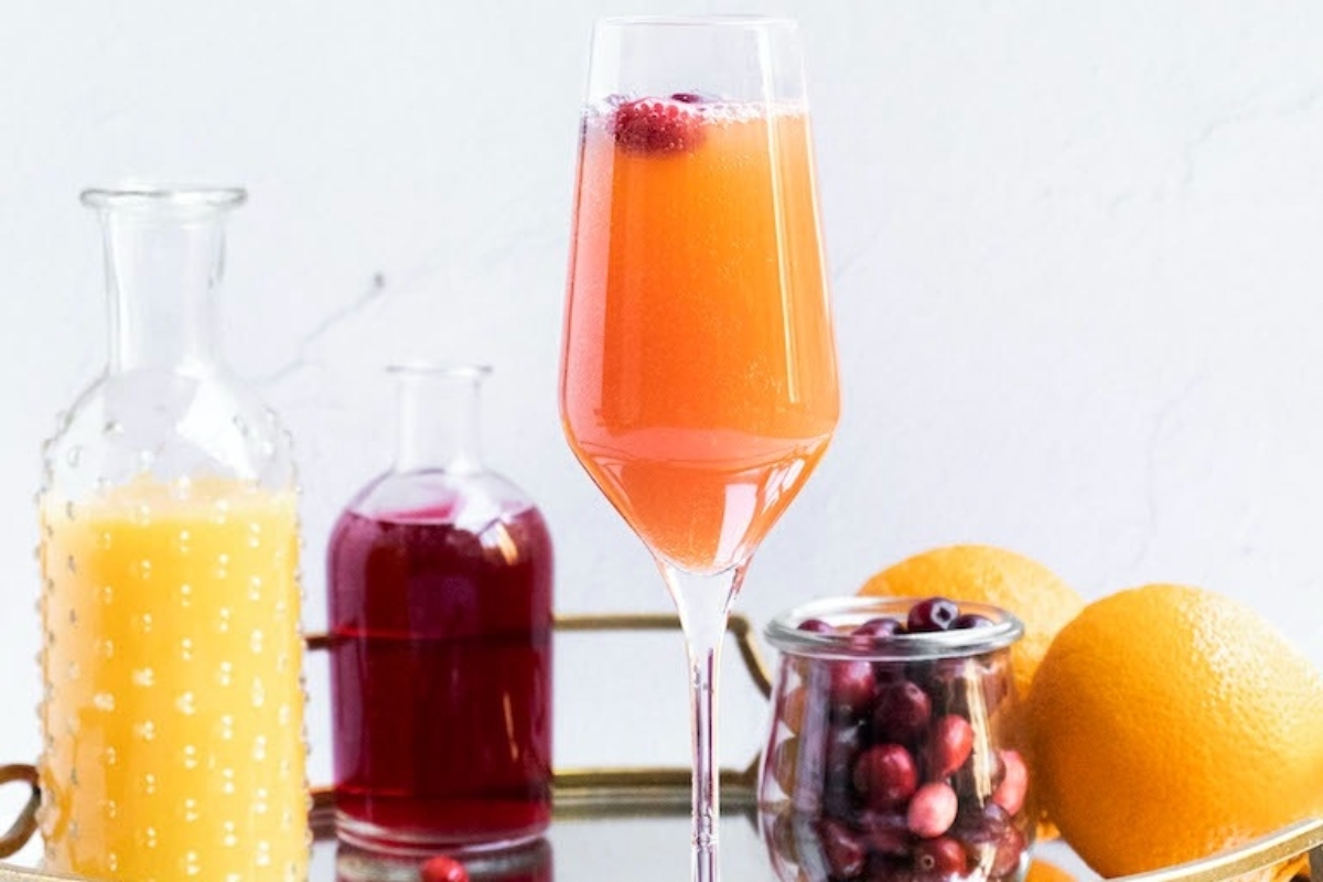 Cranberry champagne cocktail on a tray with cranberries and oranges.