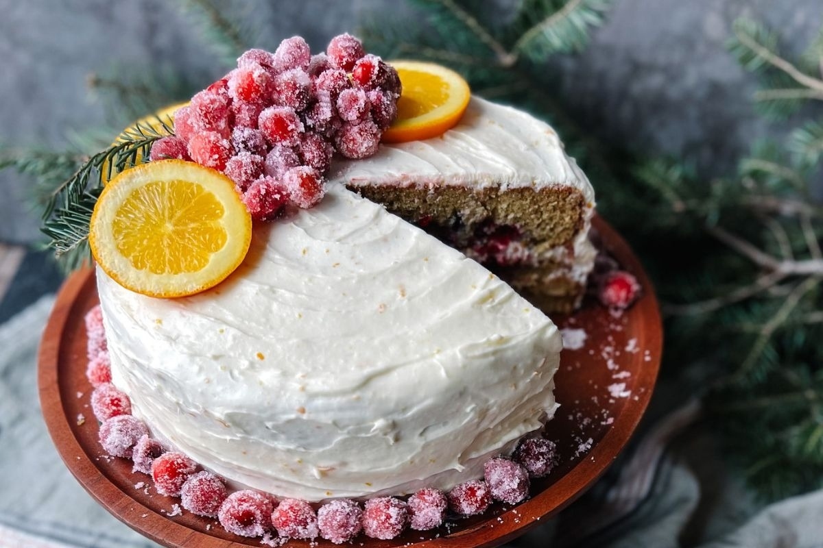 A cake with orange slices and cranberries on a wooden plate.