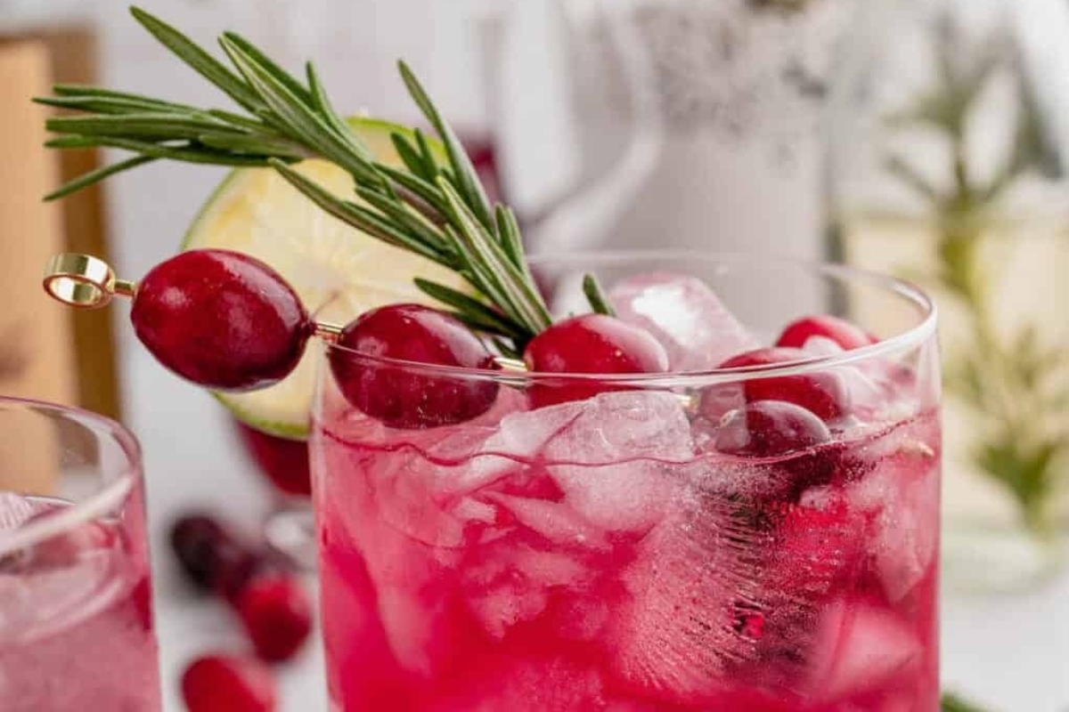 A cranberry cocktail garnished with rosemary sprigs.