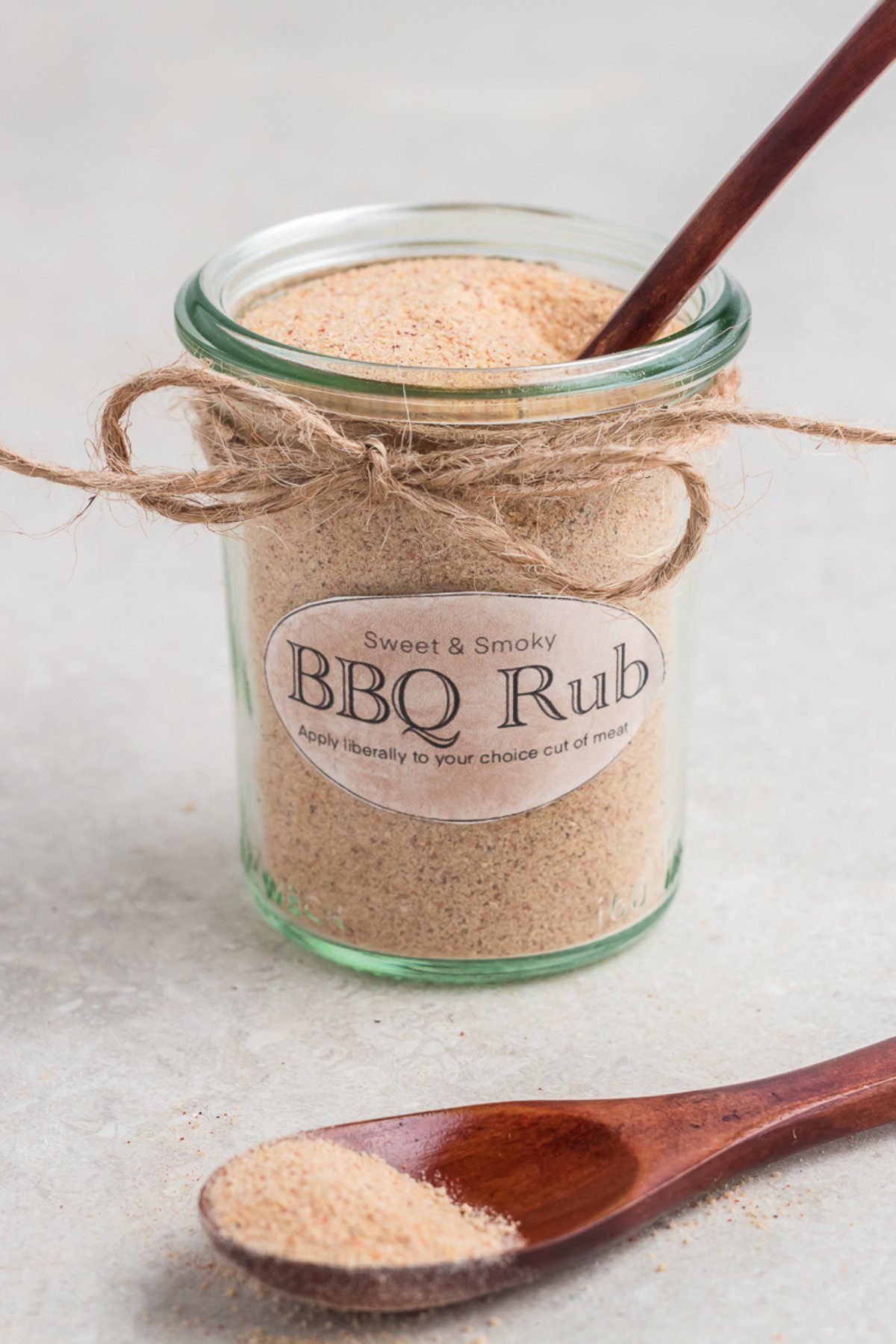 Glass jar labeled "BBQ Rub" with a wooden spoon and DIY BBQ Rub Recipe seasoning sprinkled on a light surface.