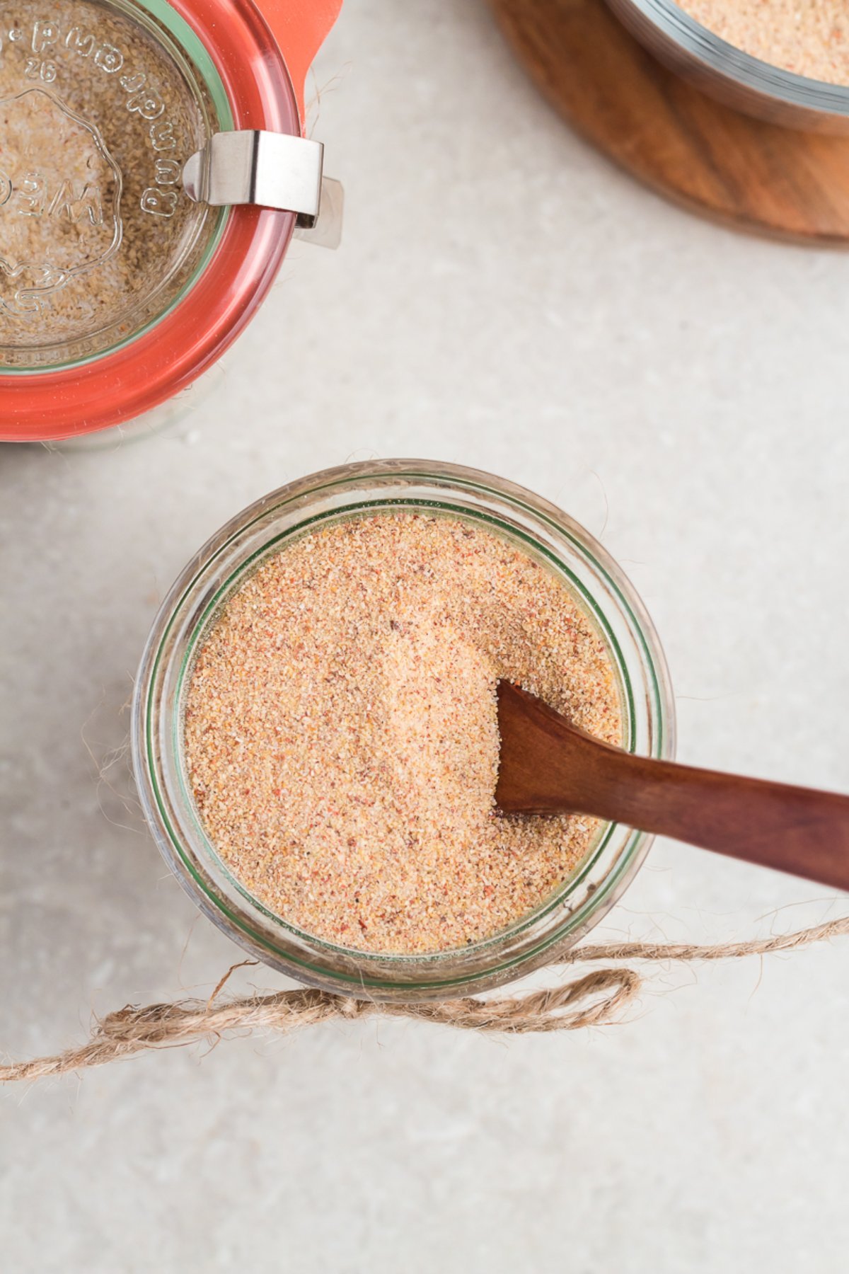 A glass jar of seasoning powder with a wooden spoon inside, placed on a light surface—perfect for storing your DIY BBQ Rub Recipe.