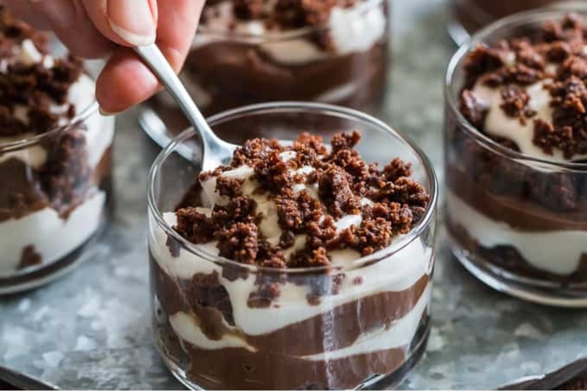 A person holding a spoon in a glass of chocolate pudding, perfect for Christmas trifle recipes.