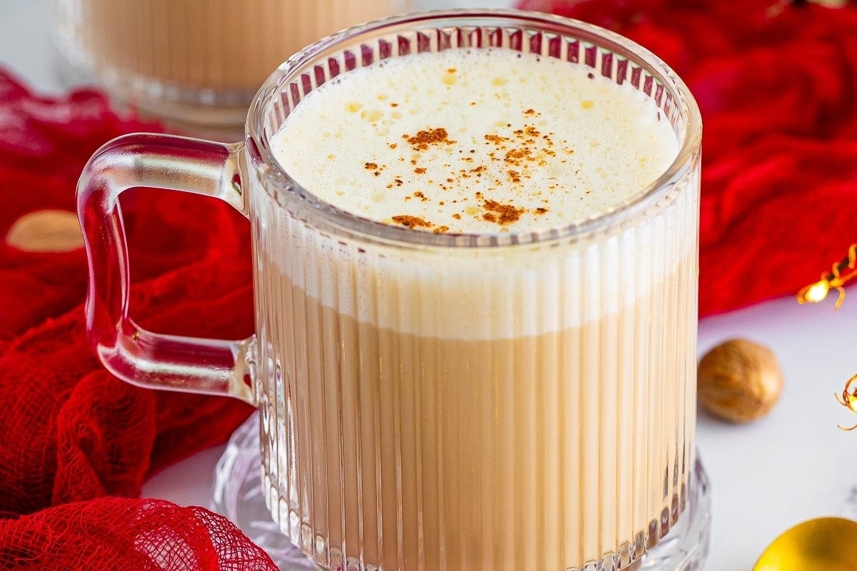 Two mugs of latte with cinnamon and nutmeg on a red cloth, perfect for eggnog lovers.
