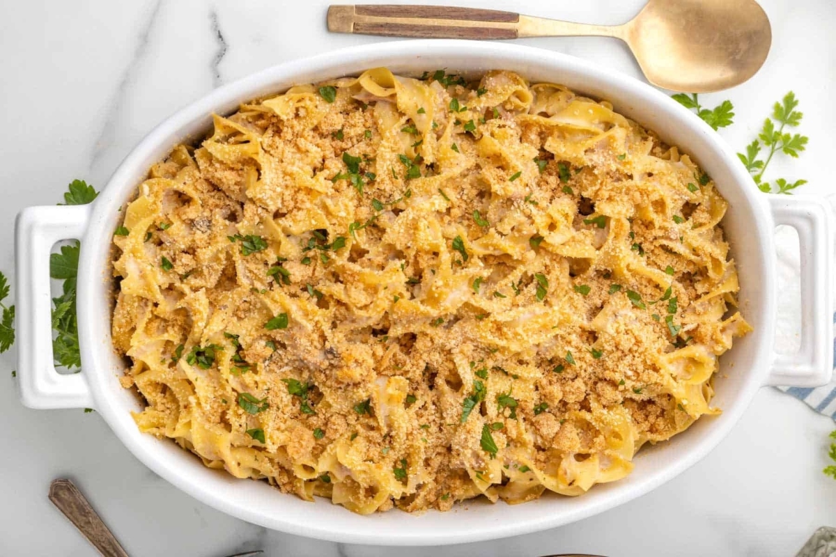 Overhead view of a creamy baked macaroni and cheese in a white casserole dish, sprinkled with breadcrumbs and garnished with parsley on a marble countertop.