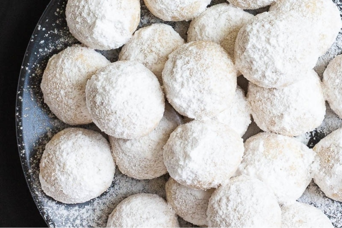 Powdered sugar cookies on a black plate.