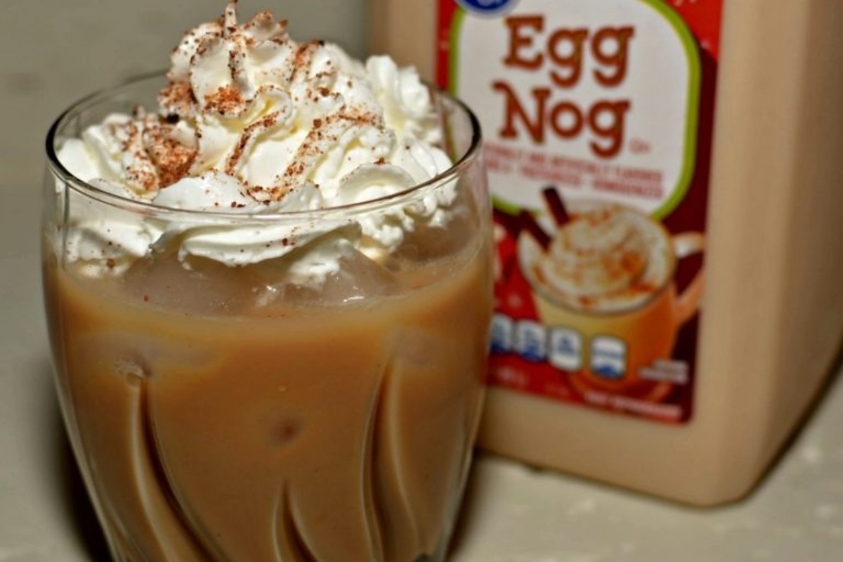 A cup of egg nog with whipped cream and a bottle of egg nog.