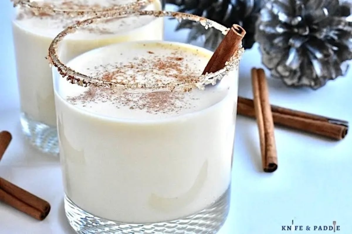 Two glasses of eggnog with cinnamon sticks.
