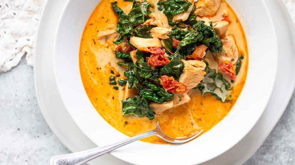 A bowl of chicken and kale soup with a spoon.
