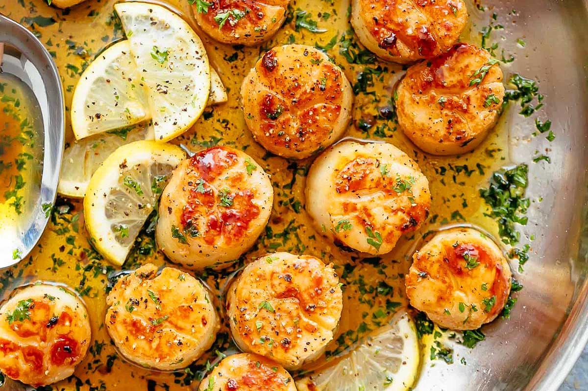 Scallops cooked in a pan with lemon slices and herbs, perfect for a feast of seven fishes.