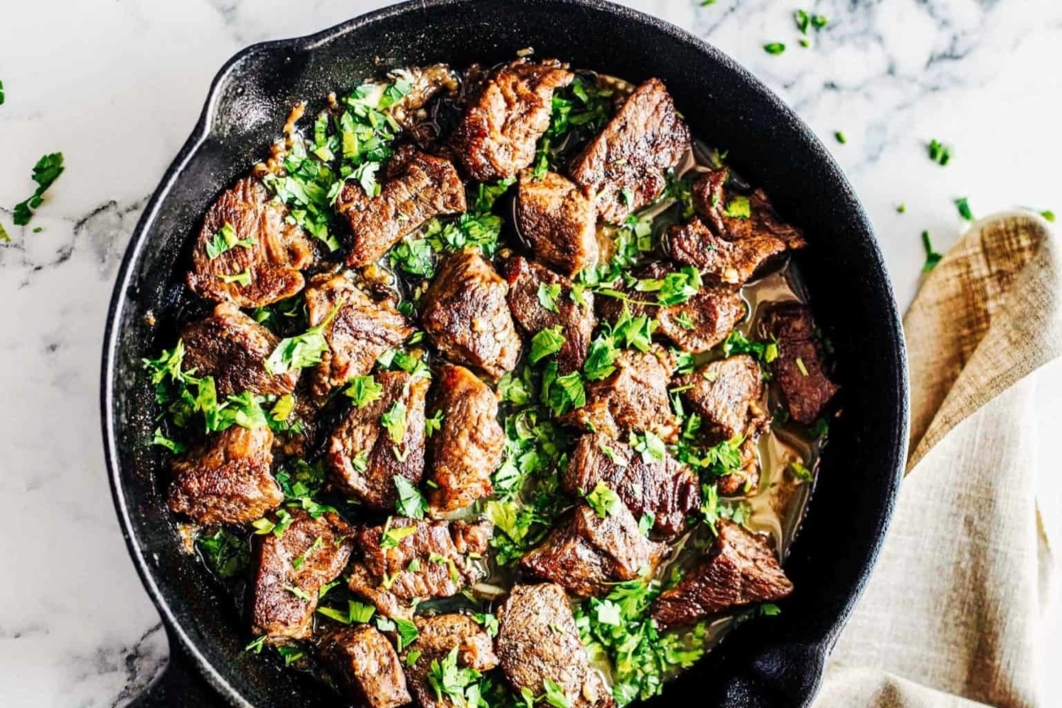 Sizzling steak in a skillet with parsley and herbs perfect for NYE appetizers.