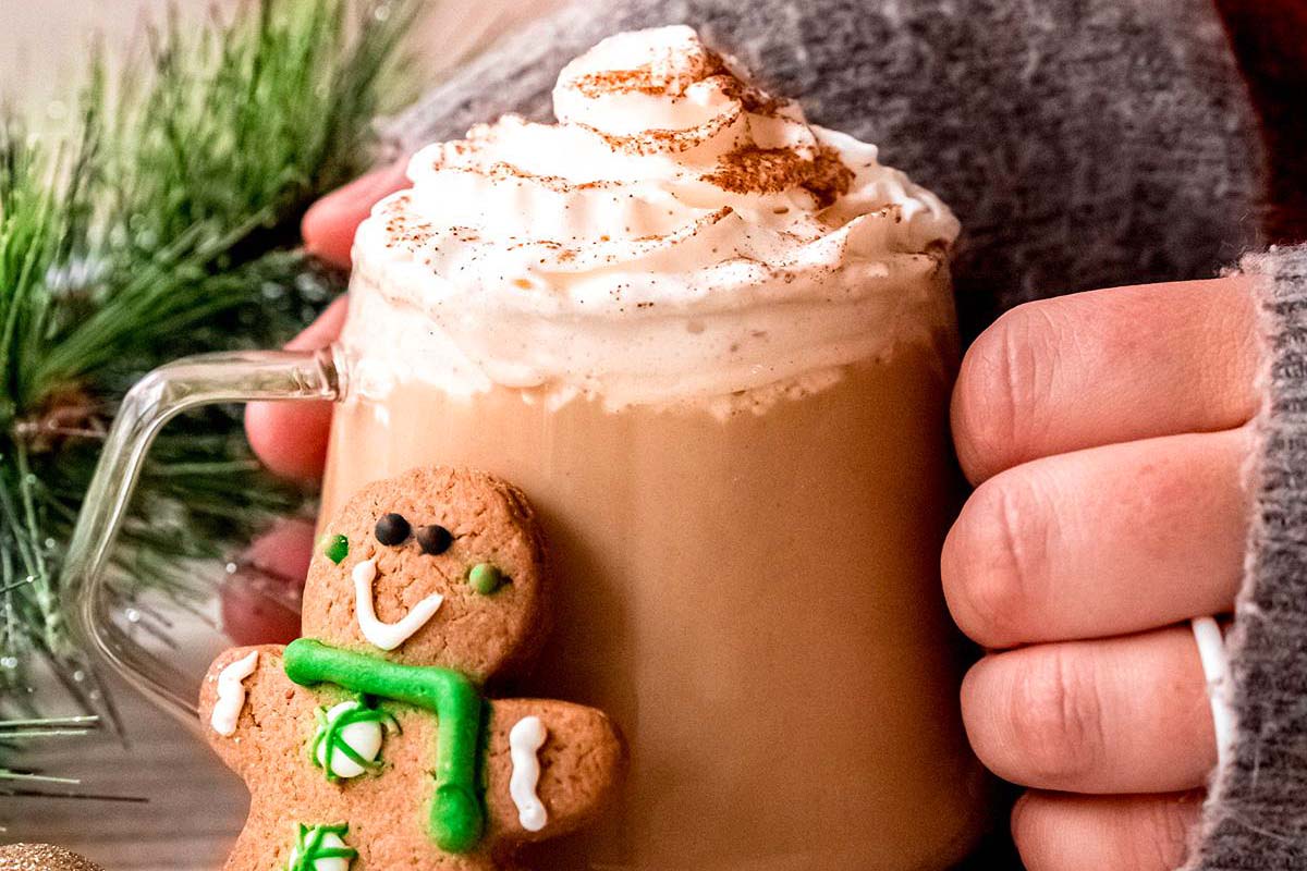 A person holding a cup of Starbucks holiday coffee with whipped cream and a gingerbread cookie.