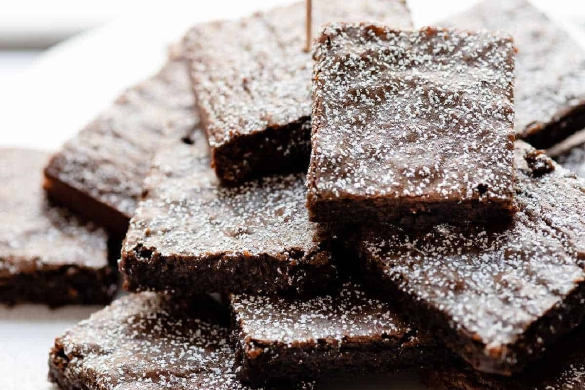 A pile of brownies with powdered sugar on a plate.