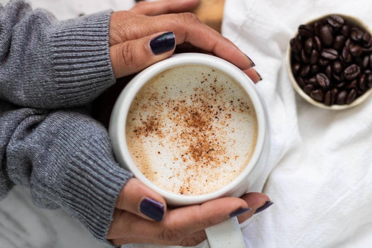 A woman's hands holding a Starbucks holiday cup of coffee with cinnamon.