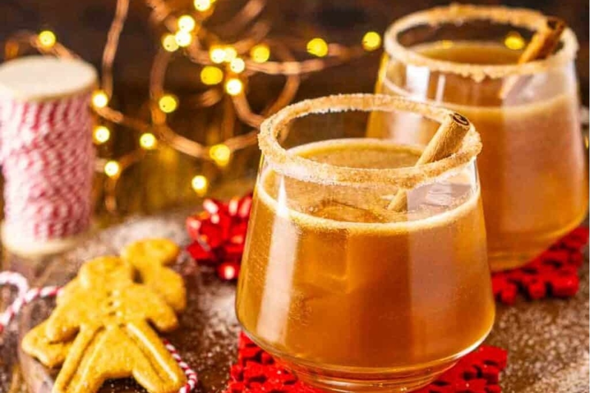 Two glasses of mulled cider with cinnamon sticks and gingerbread cookies, perfect for Christmas cocktails.
