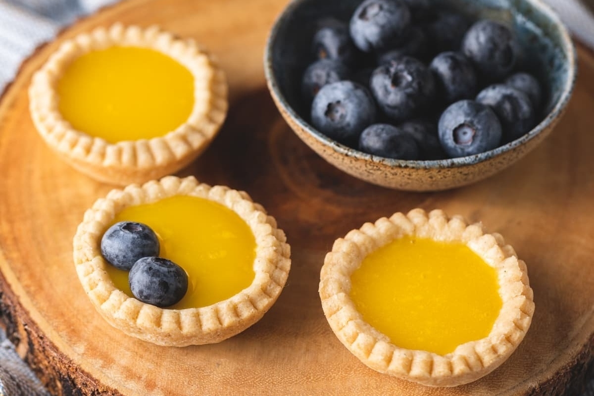 Make ahead lemon tarts with blueberries on a wooden cutting board, perfect for holiday dishes.