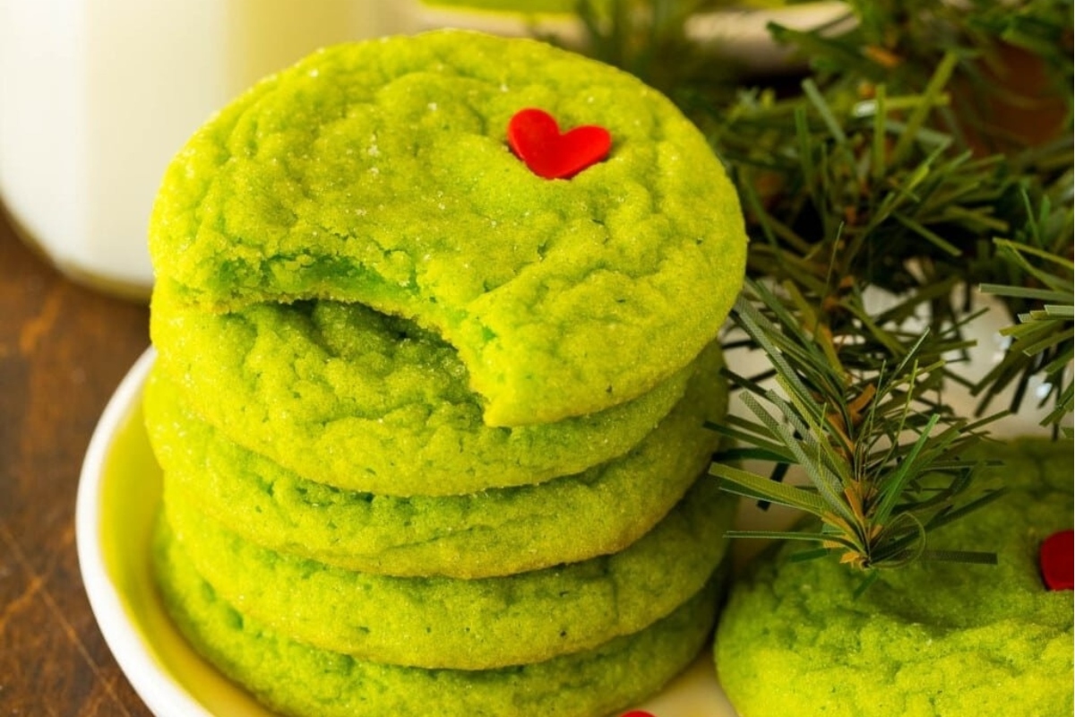 A stack of green cookies on a plate next to a glass of milk.