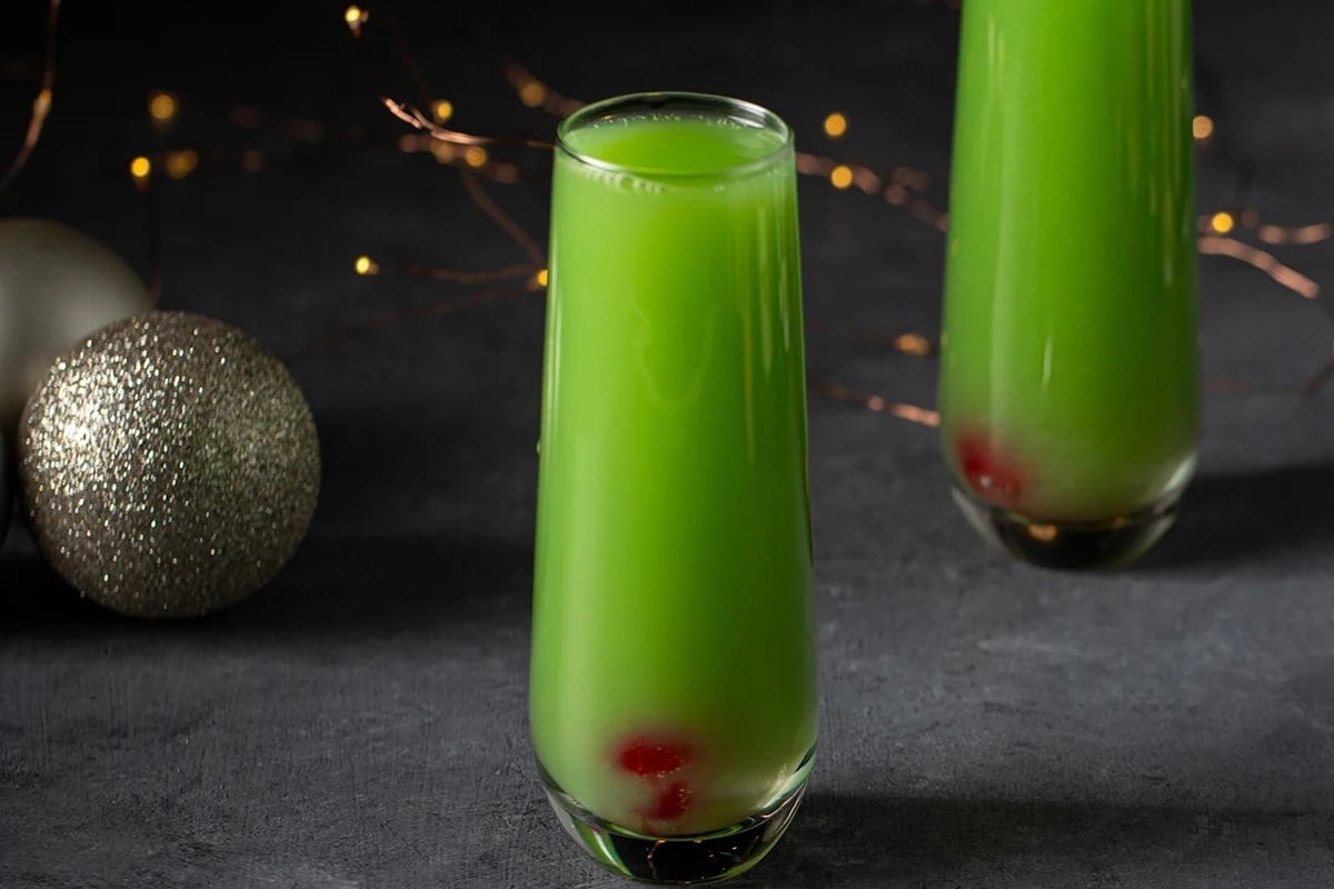 Two glasses of green liquid adorned with Christmas decorations.
