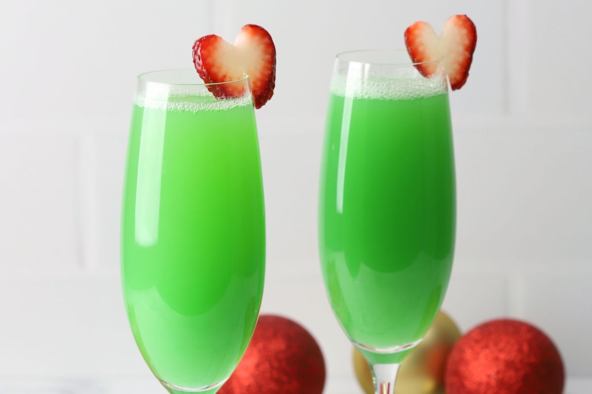 Two glasses of green Christmas drinks with strawberries in them.