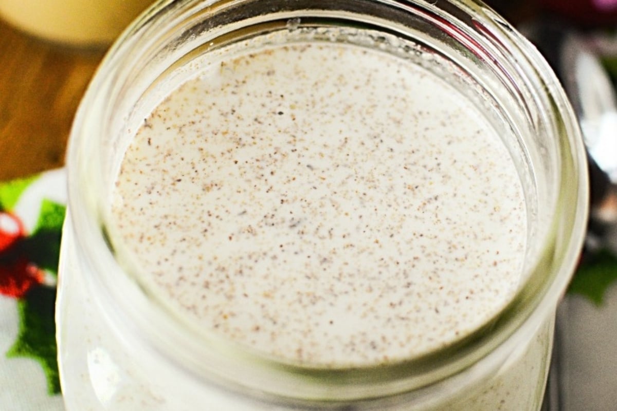 A jar of eggnog with a spoon on top of it.