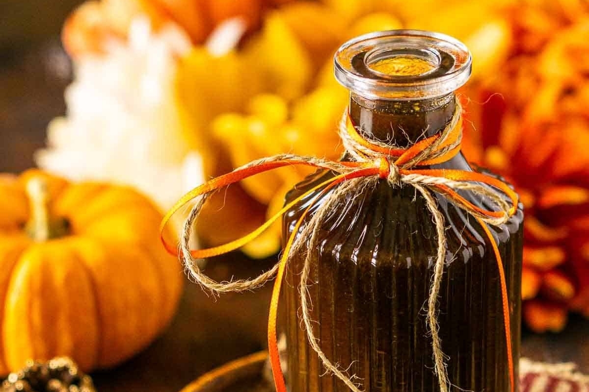 A bottle of maple syrup sitting on a table next to pumpkins, perfect for Christmas cocktails.