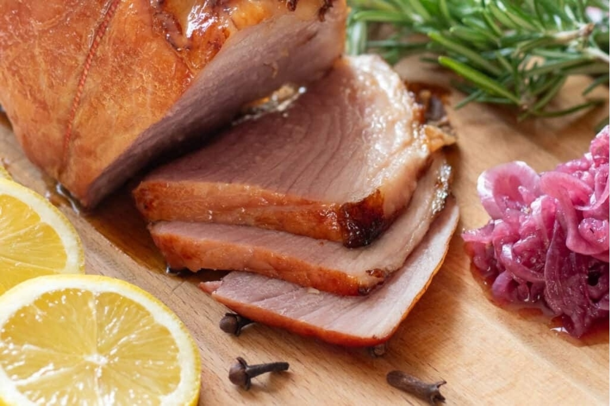 A make ahead holiday dish featuring a ham with red cabbage and lemon slices beautifully arranged on a cutting board.