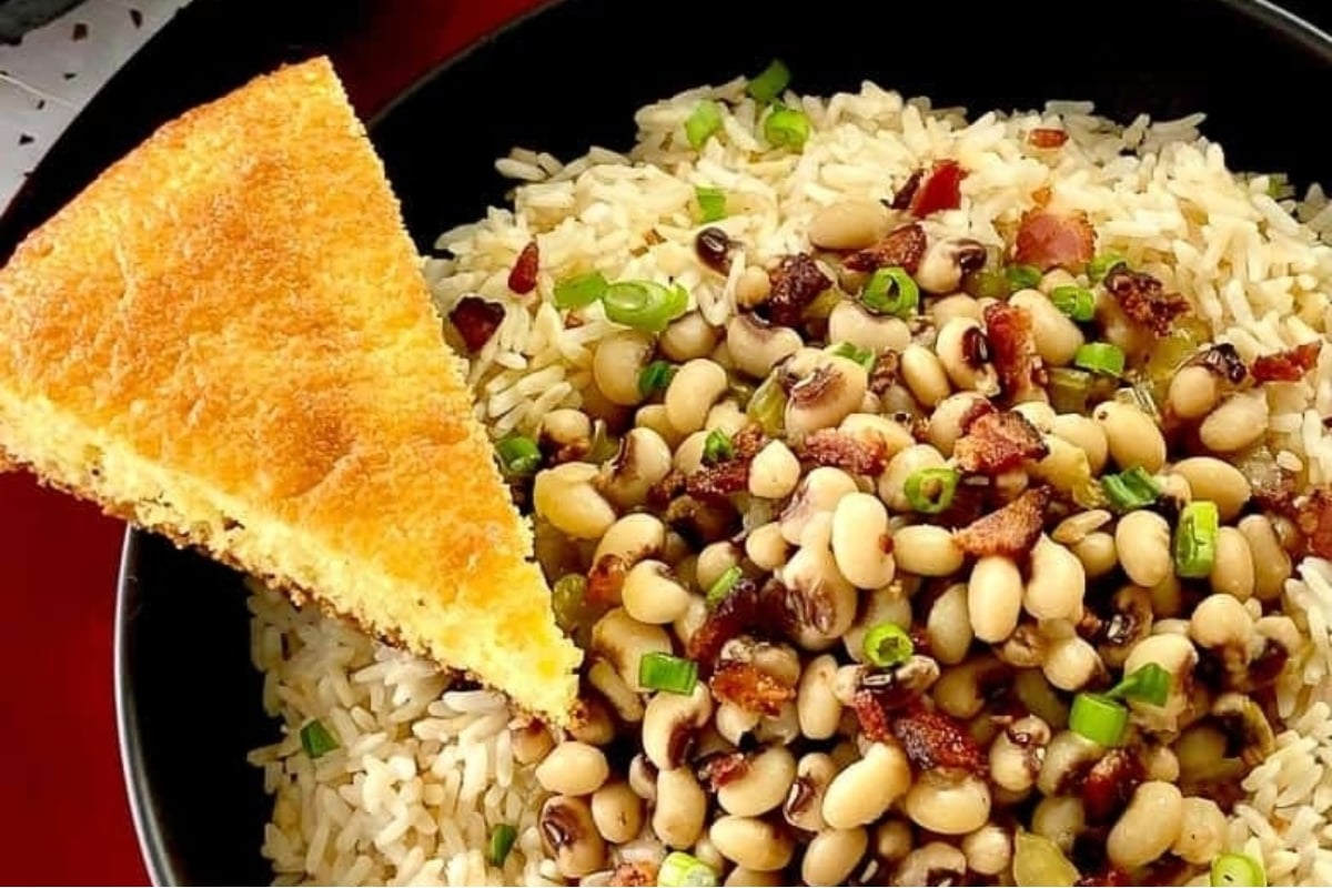 A festive New Year's dinner featuring a bowl of flavorful black eyed peas and rice accompanied by a warm piece of bread.