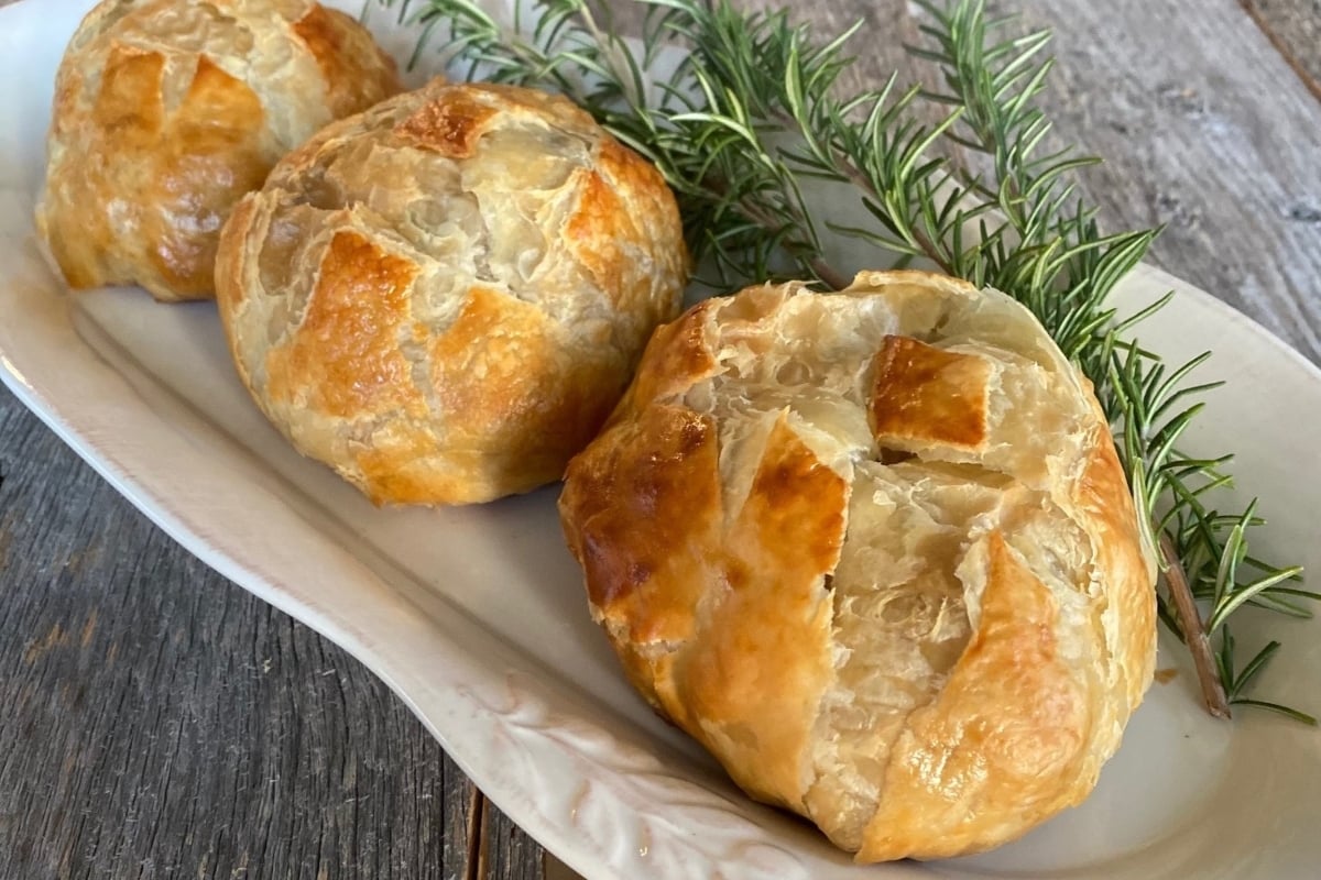 Three stuffed pastries on a plate with a sprig of rosemary, perfect for New Year's dinners.