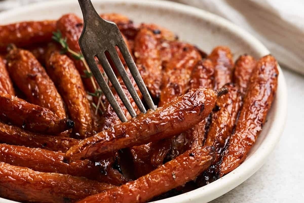 Roasted carrots in a white bowl with a fork, perfect for New Year's dinners.