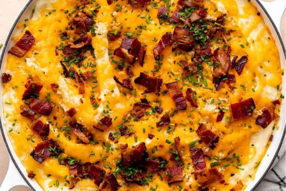 Cheesy mashed potatoes, a perfect make-ahead dish for the holidays, served in a white dish with bacon and chives.