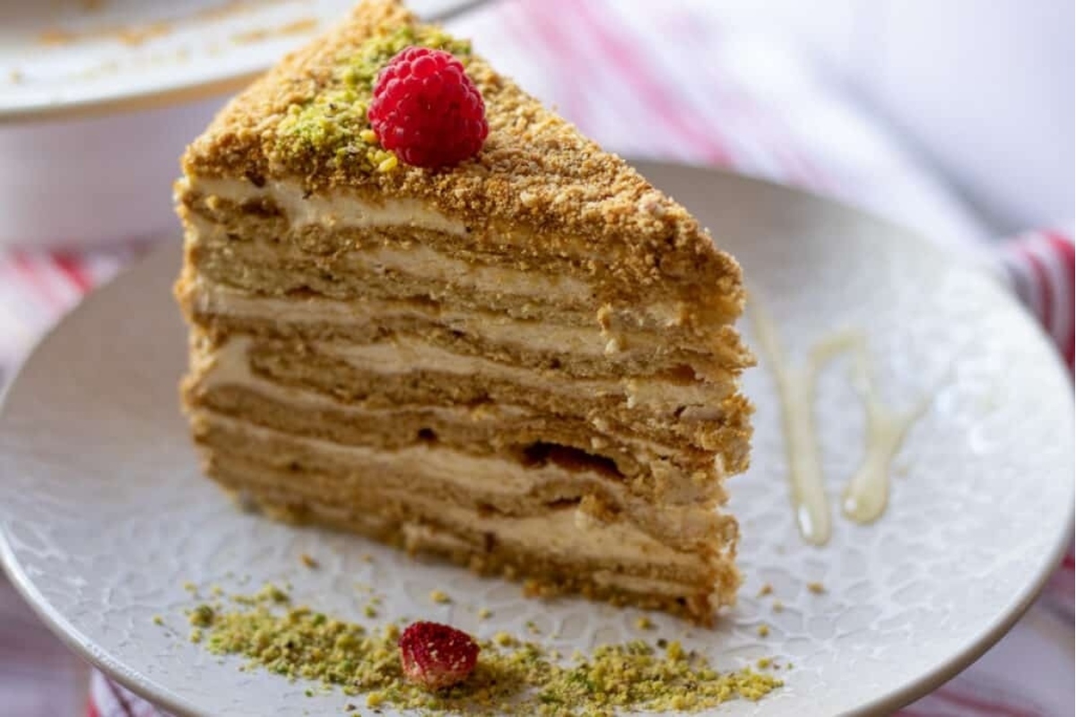 A slice of cake with raspberries and pistachios on a plate.