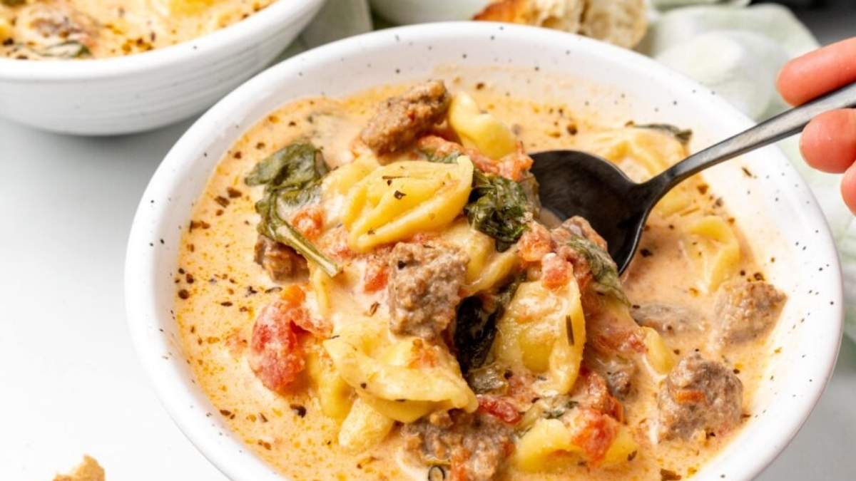 A person is holding a bowl of pasta with meat and sauce.