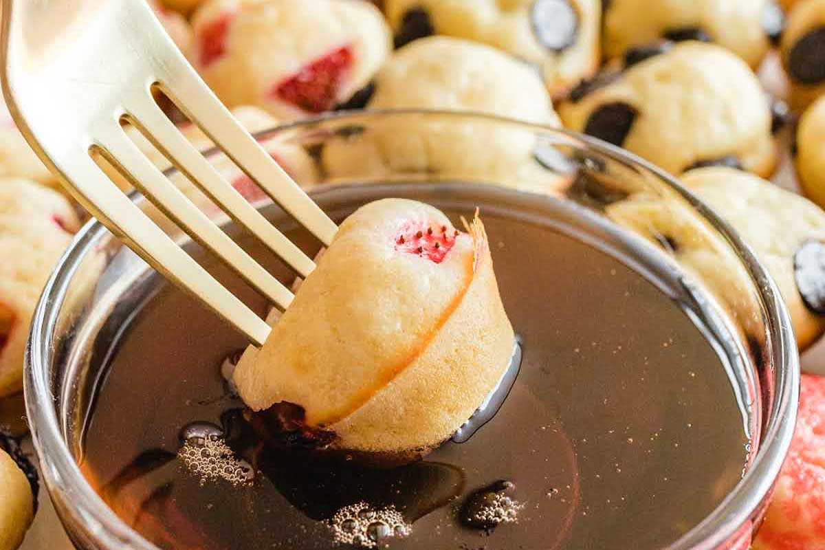During a New Year's Day Brunch, a fork is being used to dip a muffin into a chocolate sauce.