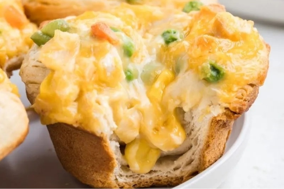 A close-up of a bread bowl filled with creamy chicken pot pie, topped with melted cheese and visible chunks of vegetables.