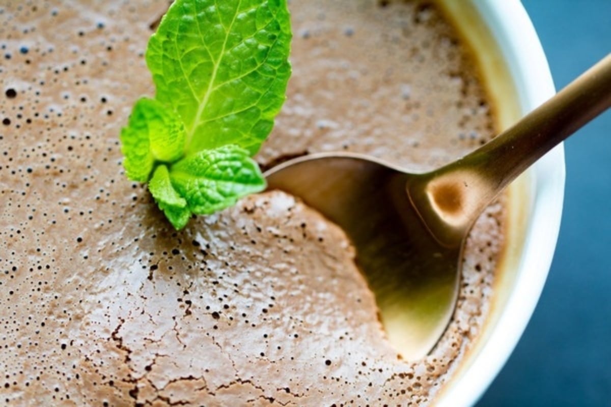A delectable bowl of chocolate mousse, adorned with a spoon and garnished with fresh mint leaves.