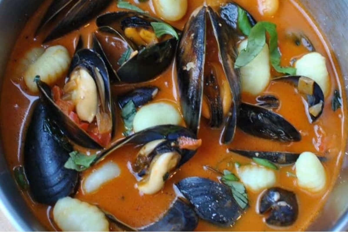 A feast of seven fishes featuring a bowl of mussels and pasta in a red sauce.