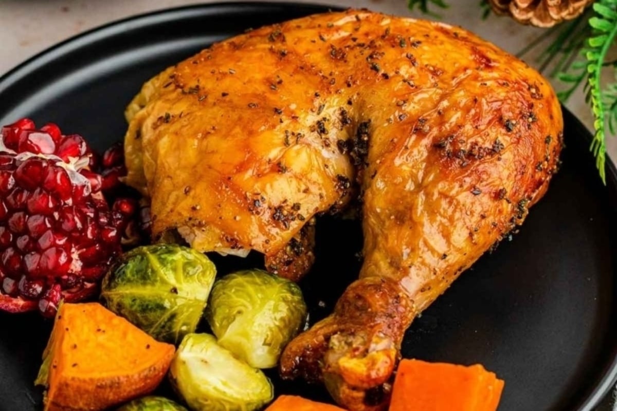 New Year's dinner featuring roasted chicken with pomegranate and brussel sprouts on a black plate.