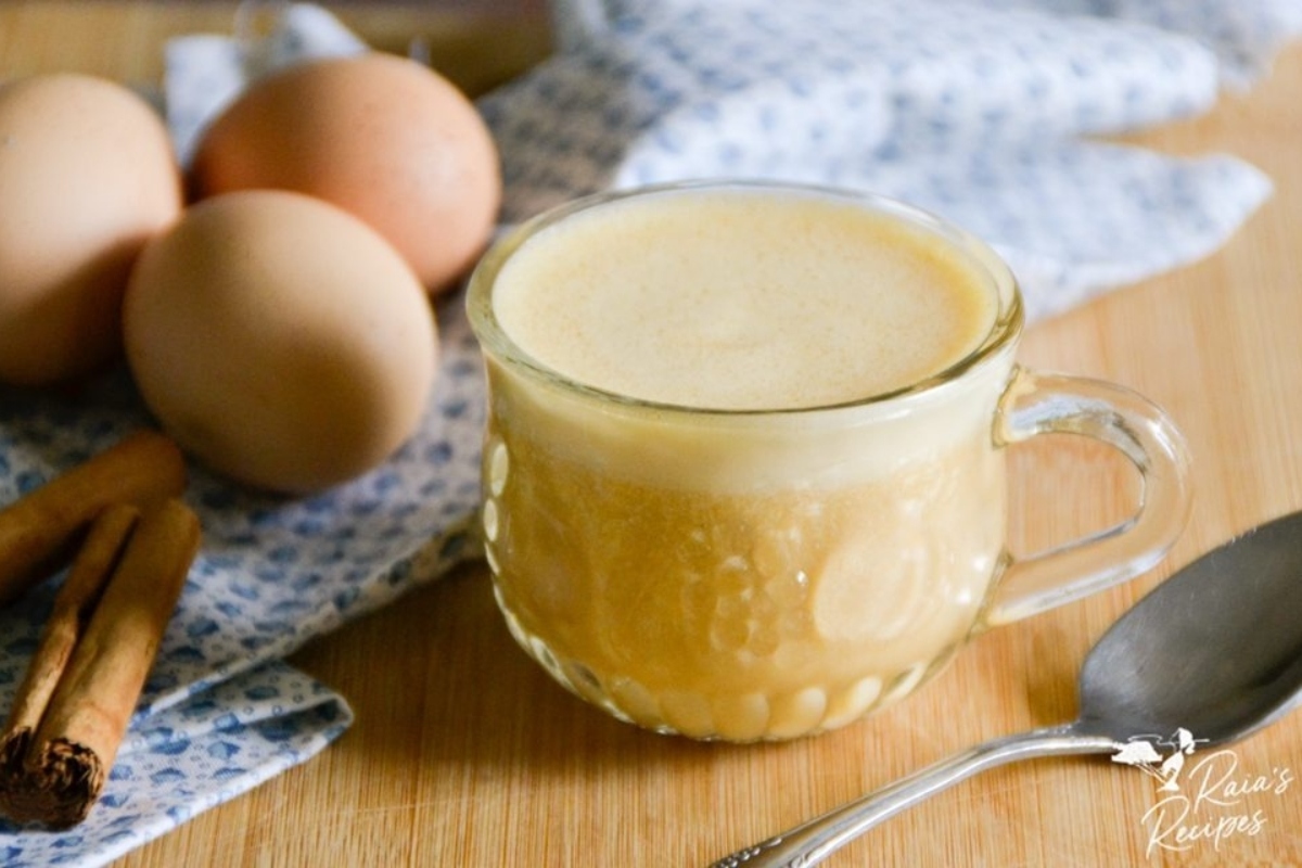 A mug with cinnamon and eggnog drinks next to it.