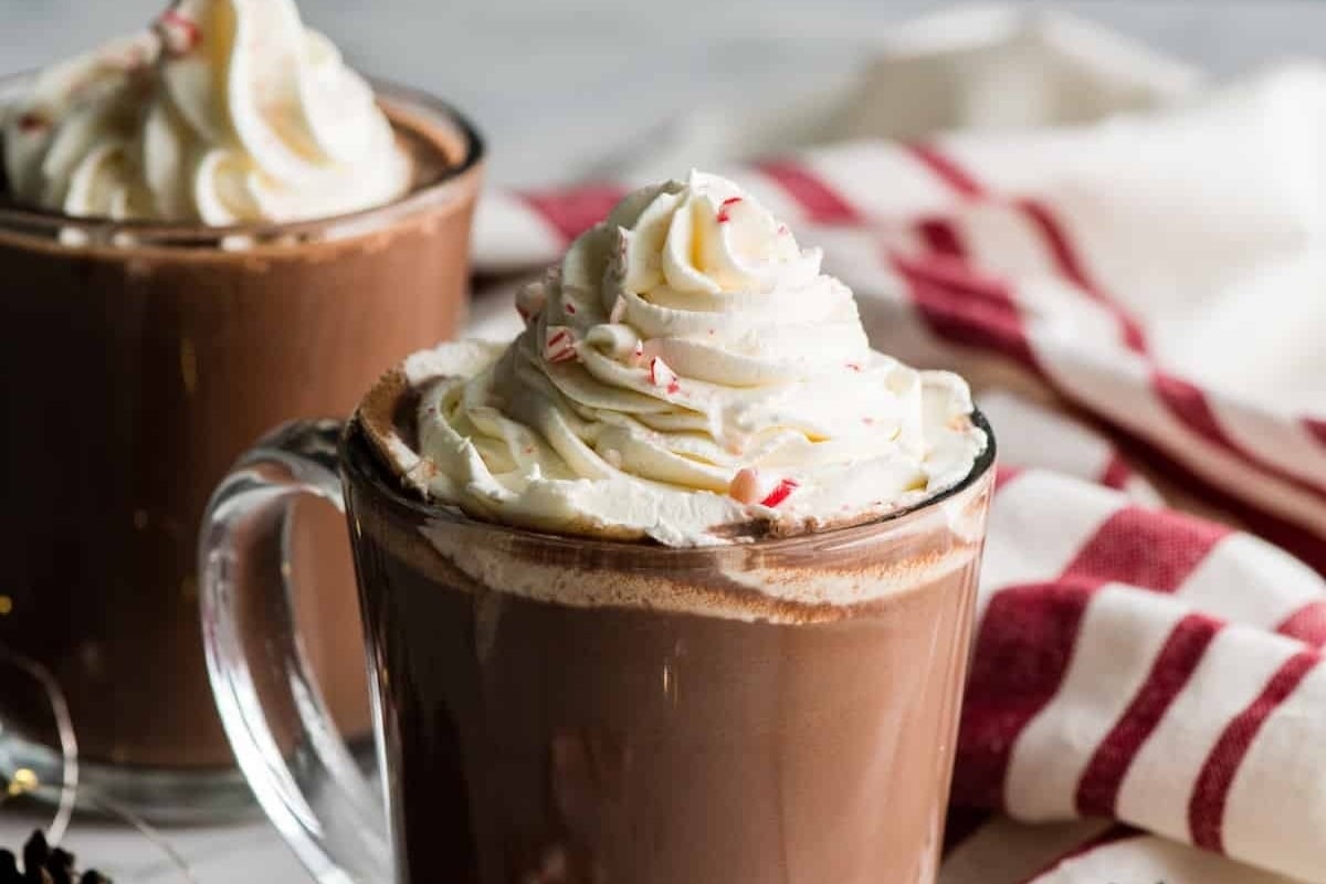 Two mugs of peppermint hot chocolate with whipped cream and candy cane recipes.