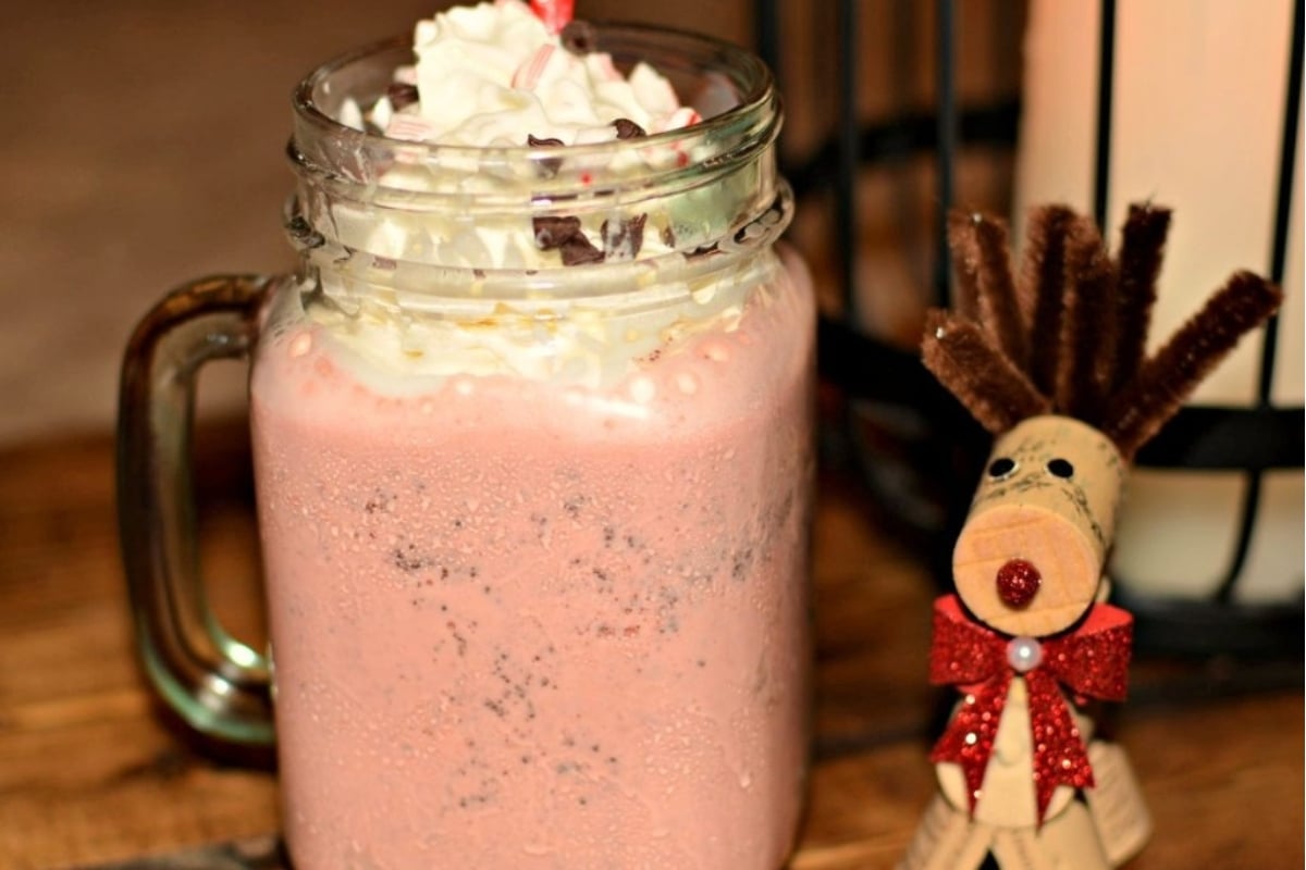 A pink milkshake in a mason jar with whipped cream and a reindeer, perfect for peppermint lovers.