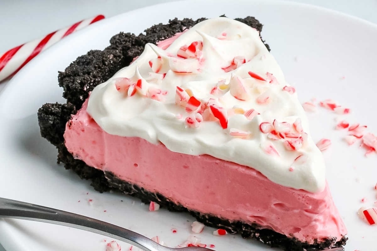 A slice of peppermint cream pie topped with a candy cane crumble on a plate with a fork.