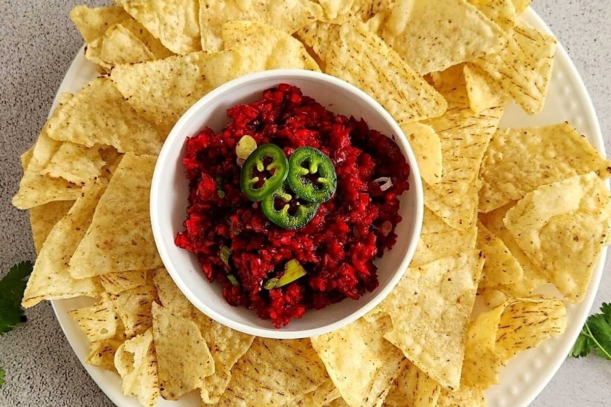 A bowl of beetroot salsa with chips on a white plate, perfect for make ahead holiday dishes.