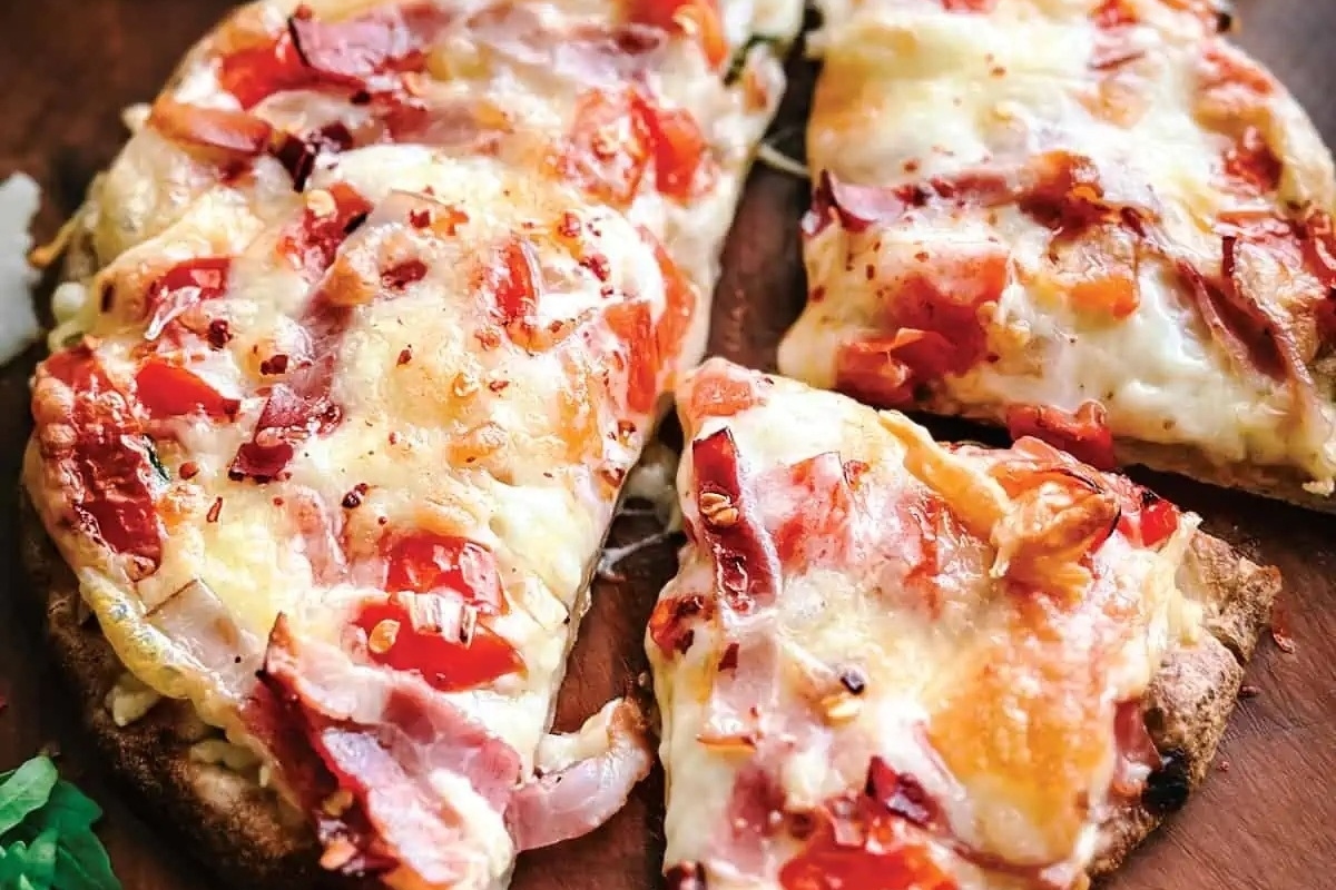 A delicious NYE appetizer, this pizza features savory ham and juicy tomatoes, elegantly presented on a wooden cutting board.