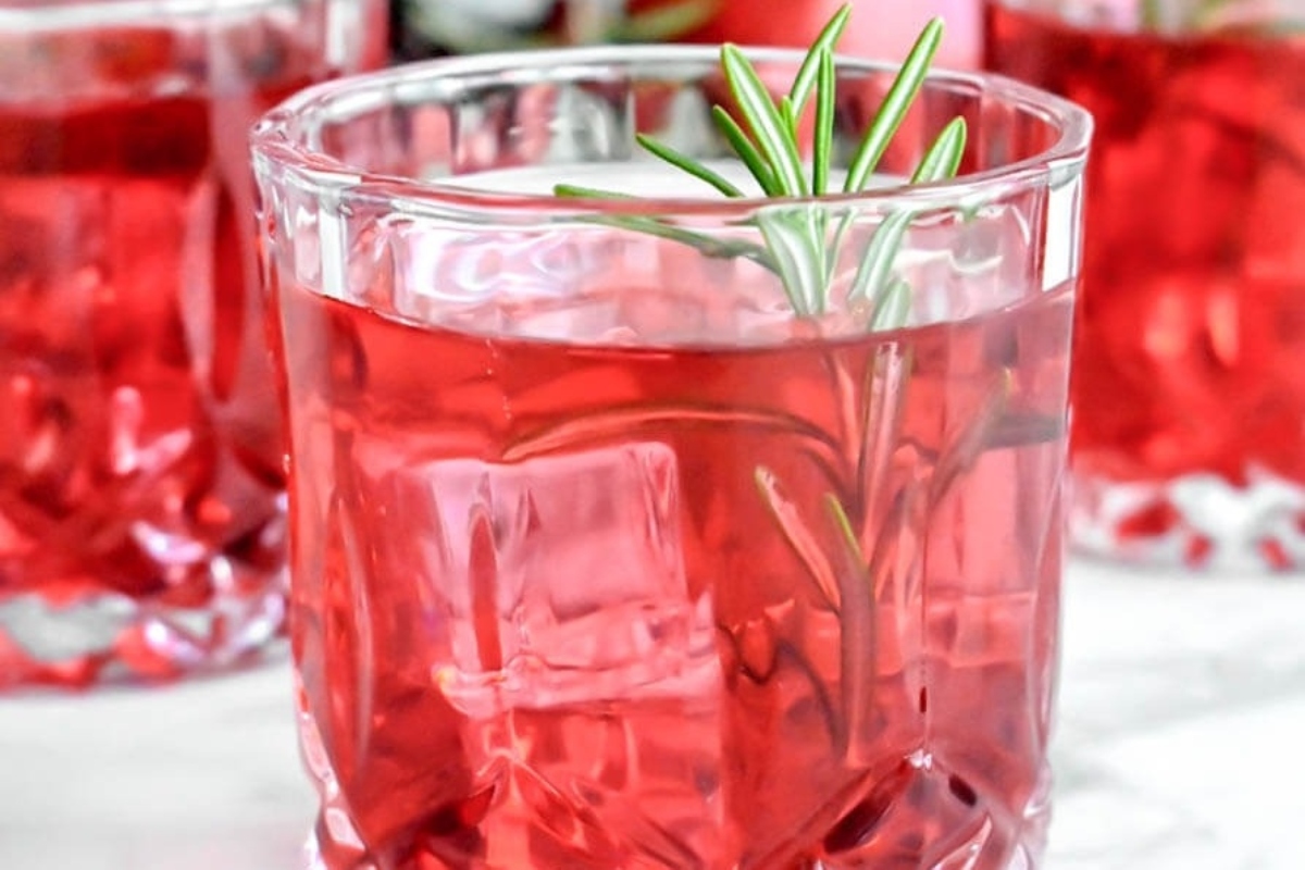 Enjoy a festive glass of red drink with a sprig of rosemary, perfect for New Year's Eve cocktail ideas.