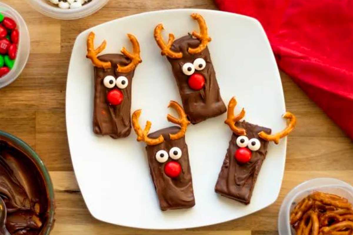 Chocolate reindeer graham crackers on a plate with candy and pretzels, perfect for reindeer treats.