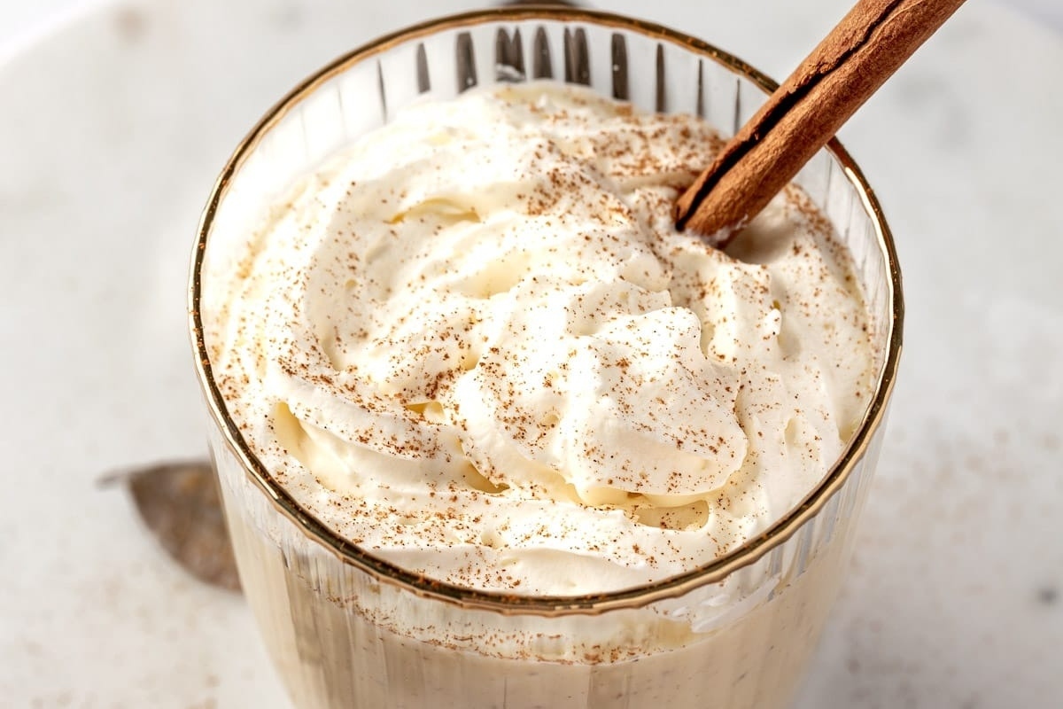 Whipped cream and cinnamon in a glass with a cinnamon stick, perfect for eggnog lovers.