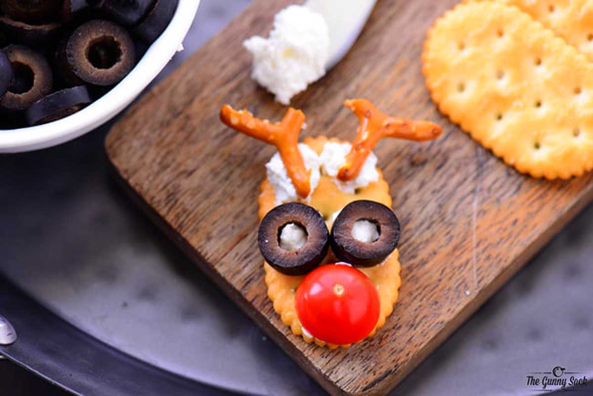 Reindeer treats black olives as eyes on a cracker a cutting board.