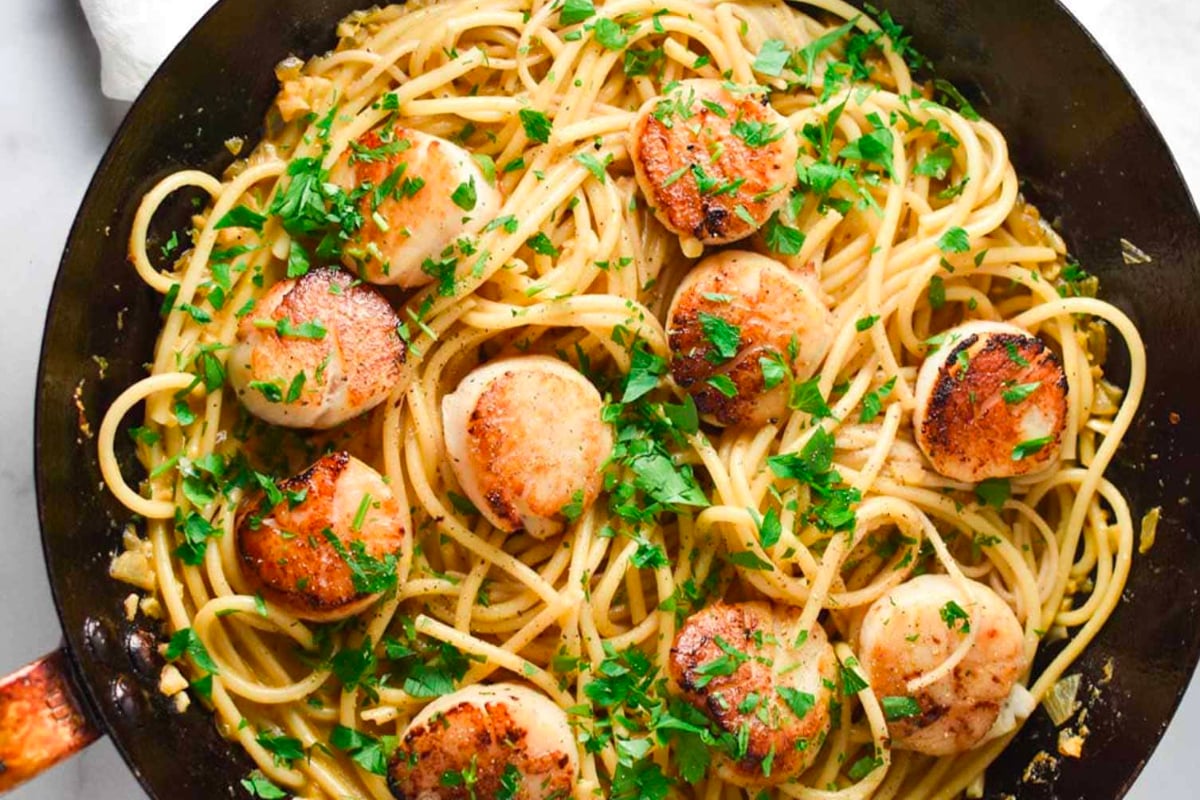 Scallops cooked in a skillet with parsley, perfect for elegant New Year's dinners.